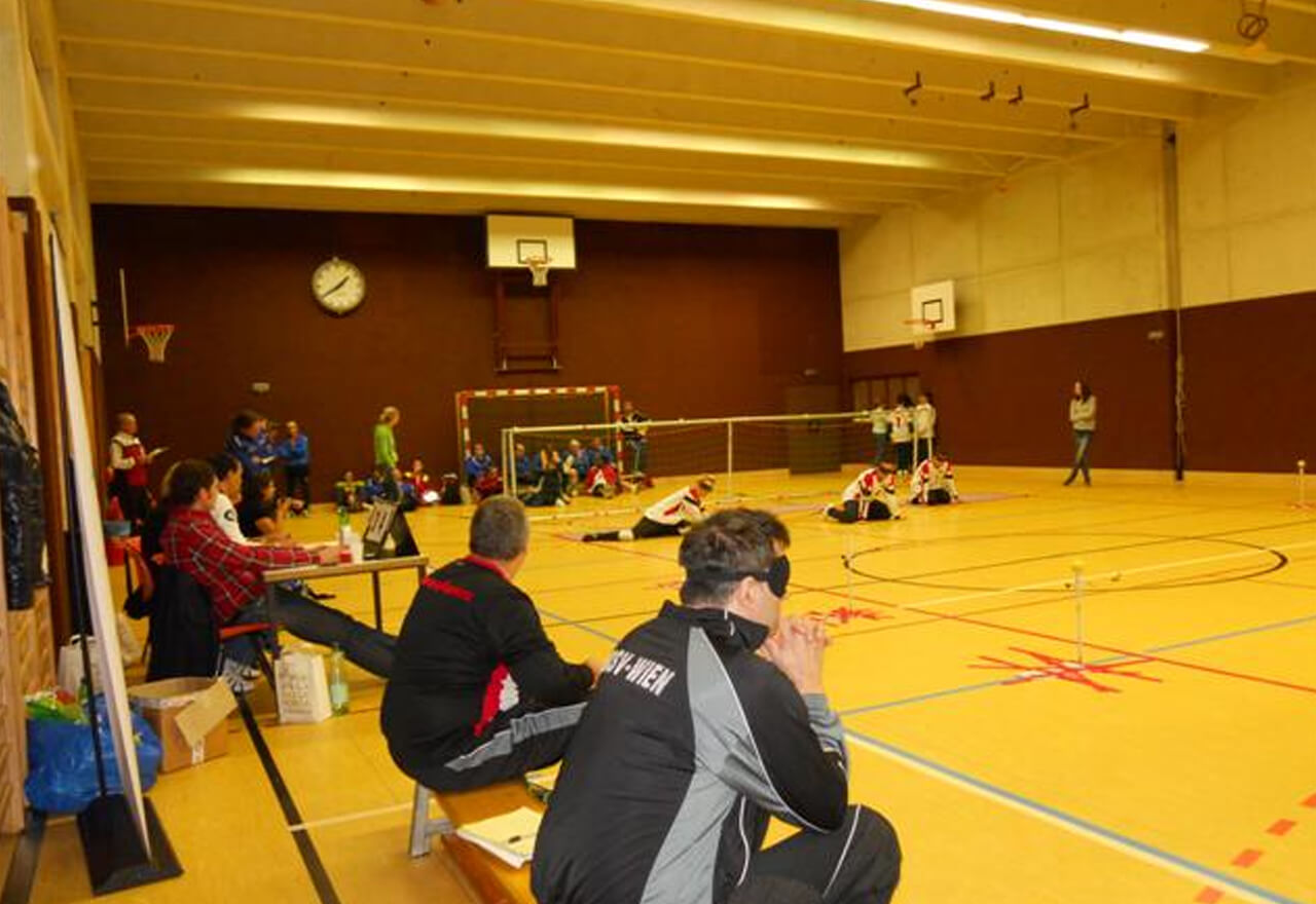 Das Torball-Spielfeld von der Seitenbank aus gesehen. Zwei SpielerInnen sitzen mit dem Rücken zur Kamera.