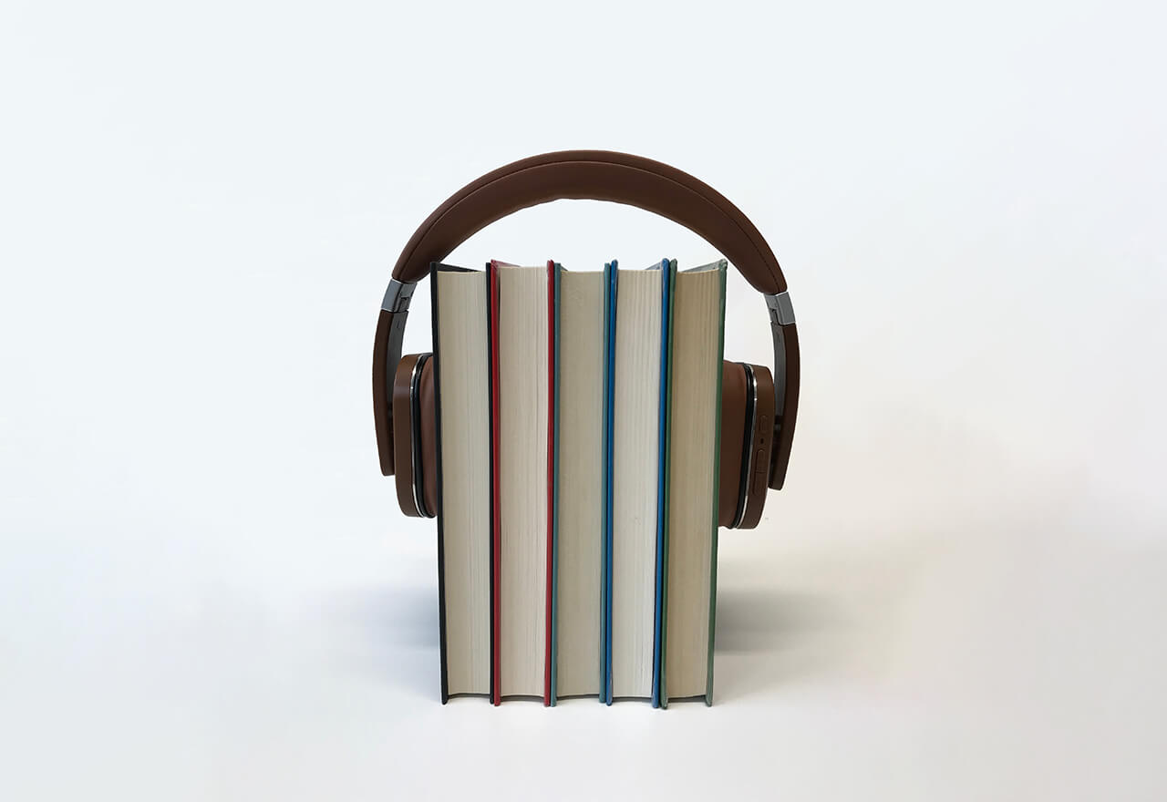 Nebeneinander stehende Bücher die zusammen Kopfhörer tragen.