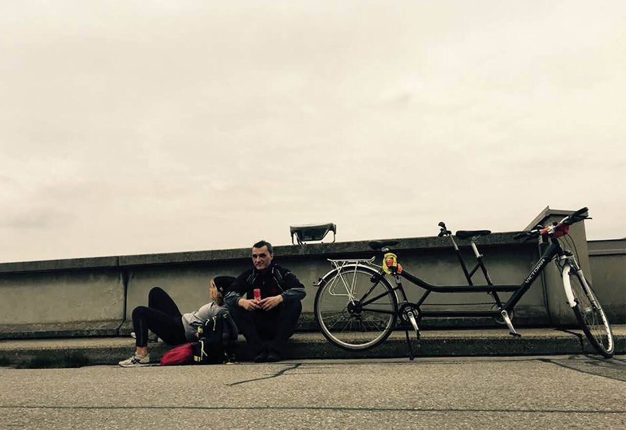 Harald und ein Bekannter sitzen auf einem Randstein, neben ihnen ein Tandem Fahrrad.