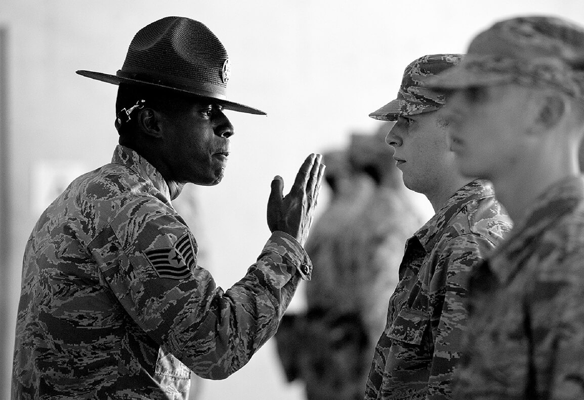 Schwarz-Weiss Foto von einem Army-Offizier der mit erhobender Hand vor einer Reihe Soldaten steht