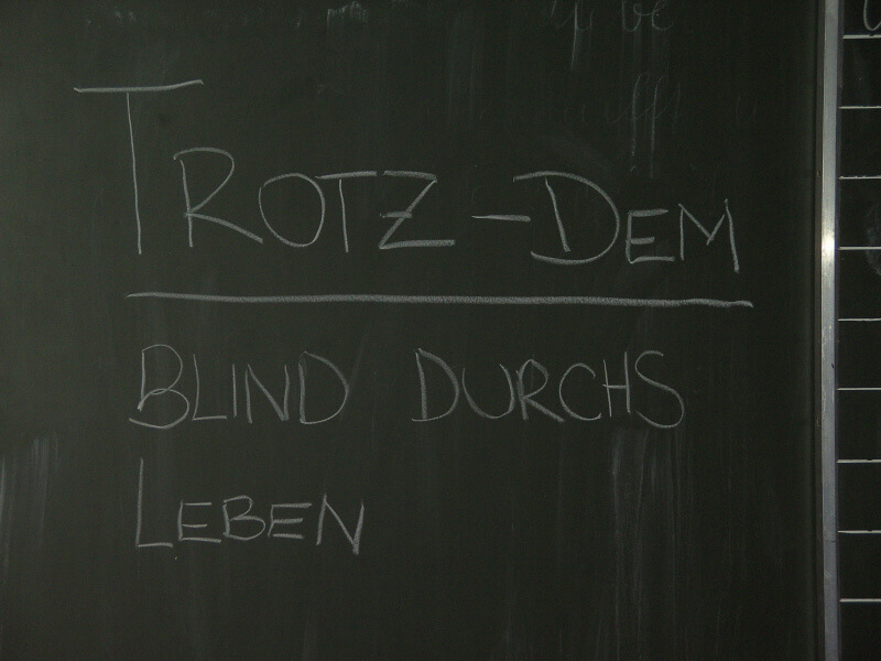 TROTZ-DEM – Blind durch's Leben auf eine Tafel geschrieben.
