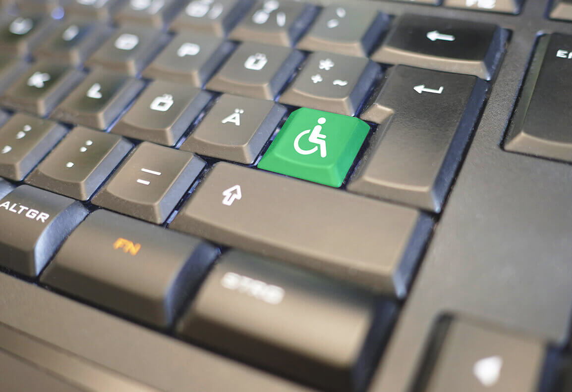 Foto einer schwarzen Tastatur. Eine Taste ist grün. Darauf befindet sich das Symbol für RollstuhlfahrerInnen.