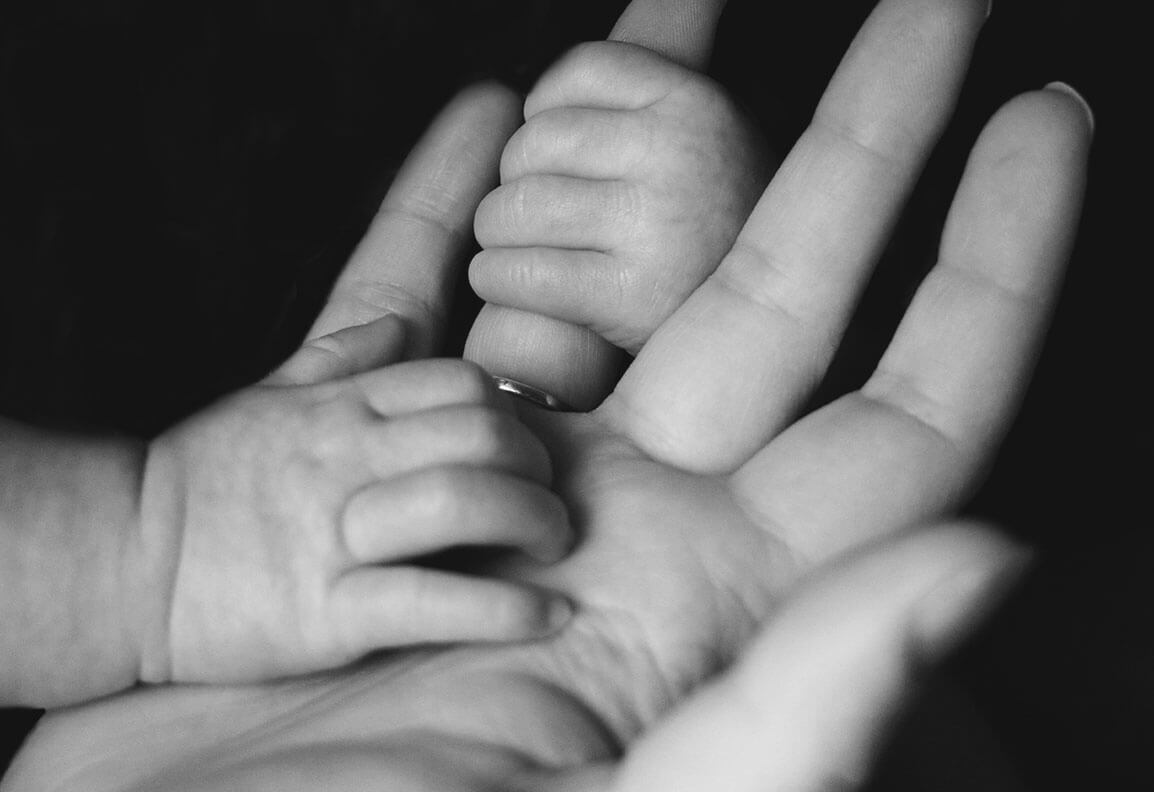 Schwar-weiß-Foto von zwei Baby-Händen die eine große Hand festhalten.