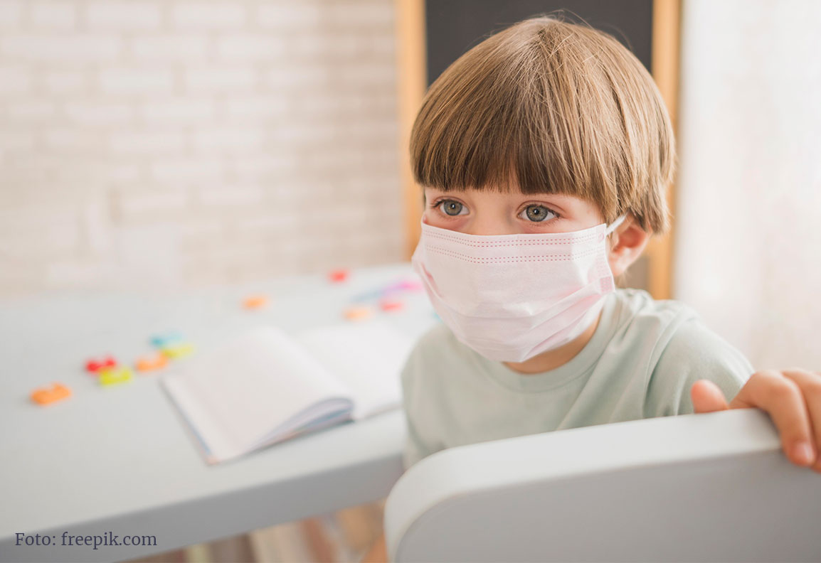Schulkind mit Atemschutzmaske vor einem Schulbuch